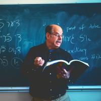 David Forman in front of a blackboard with Yiddish on the board