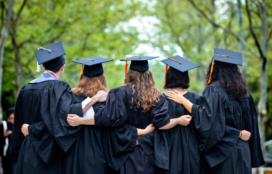 students outside in graduation cap and gowns, arms linked
