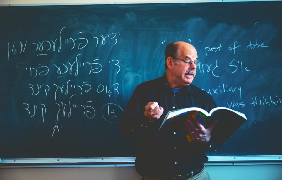 David Forman in front of a blackboard with Yiddish on the board