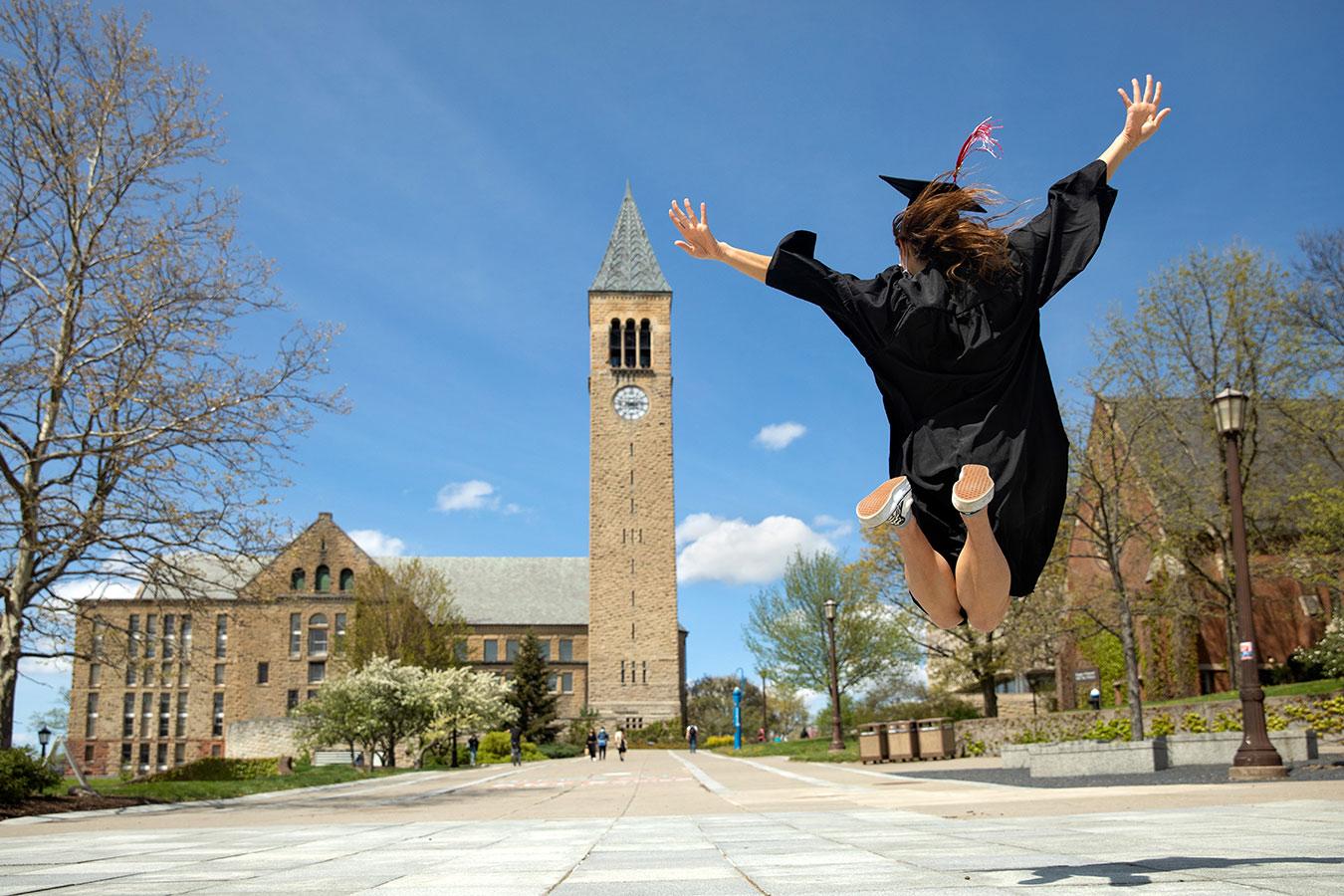 Student in cap and gown jumping with McGraw Clock Tower in the background